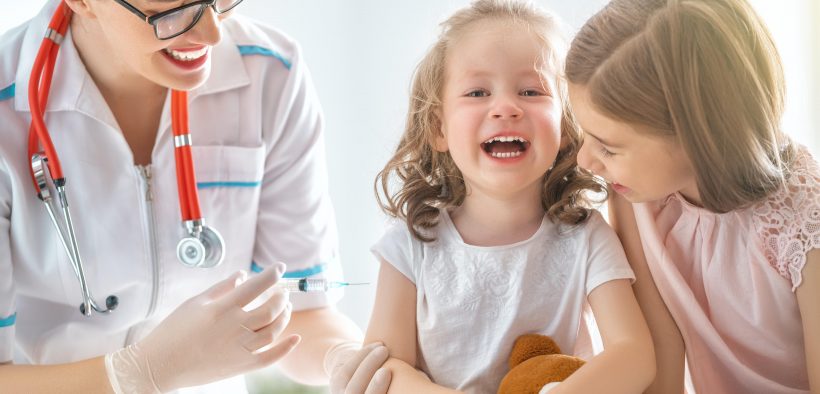 dwie uśmiechające się dziewczynki podczas szczepienia wraz z pania doktor
