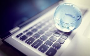 mała, kryształowa kula ziemska leżąca na klawiaturze laptopa