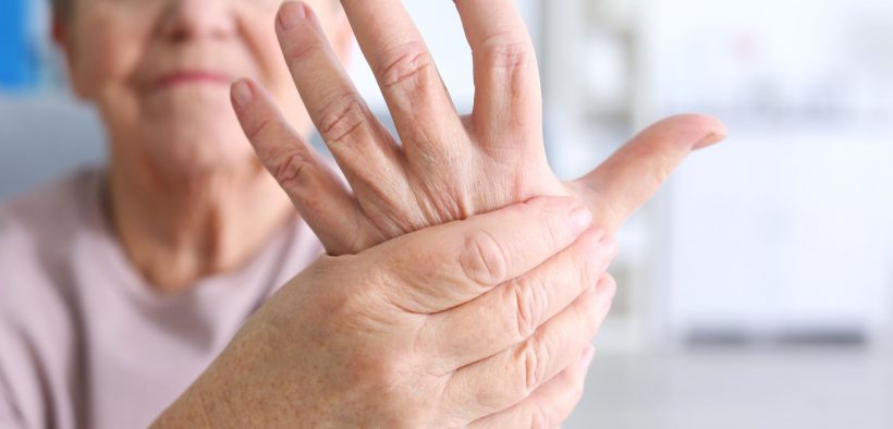 Starsza kobieta z reumatoidalnym zapaleniem stawów trzymająca się za dłoń,